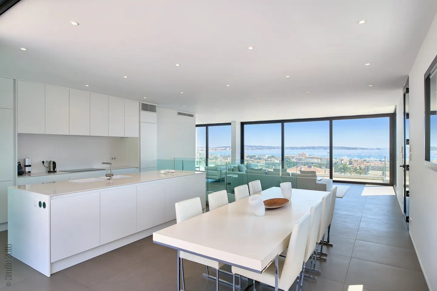 White dining table and island kitchen, glazing overlooking the sea