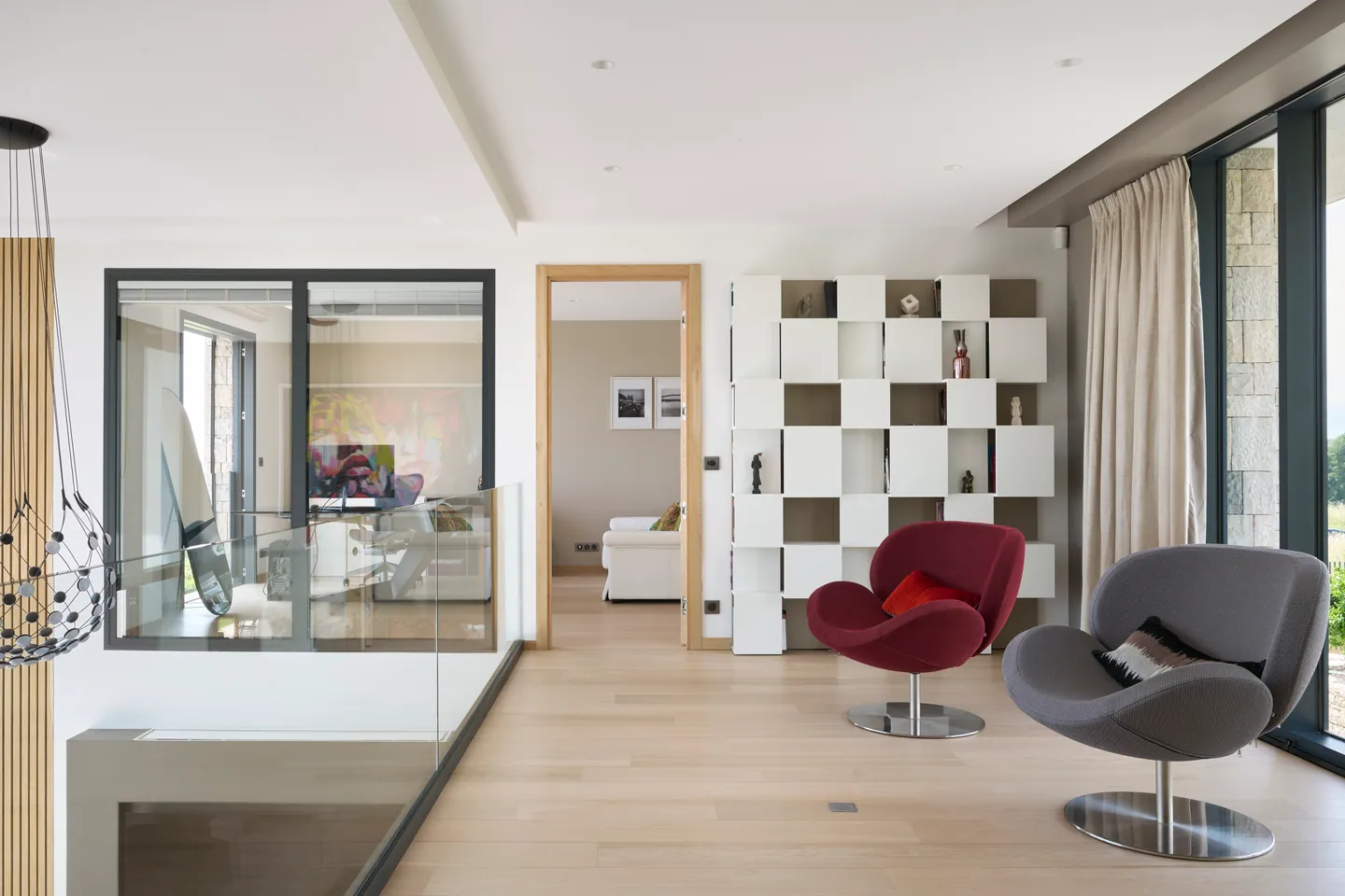 Palier de l'étage avec fauteuils design, bibliothèque blanche et garde-corps en verre