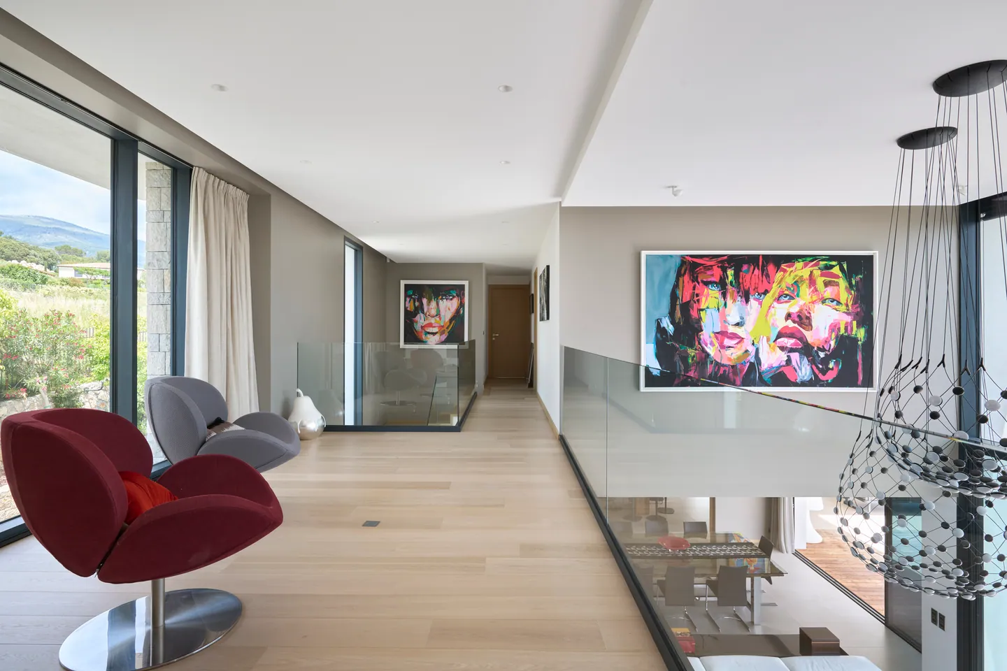Galerie en mezzanine bordée de verre, parquet clair et grands tableaux colorés