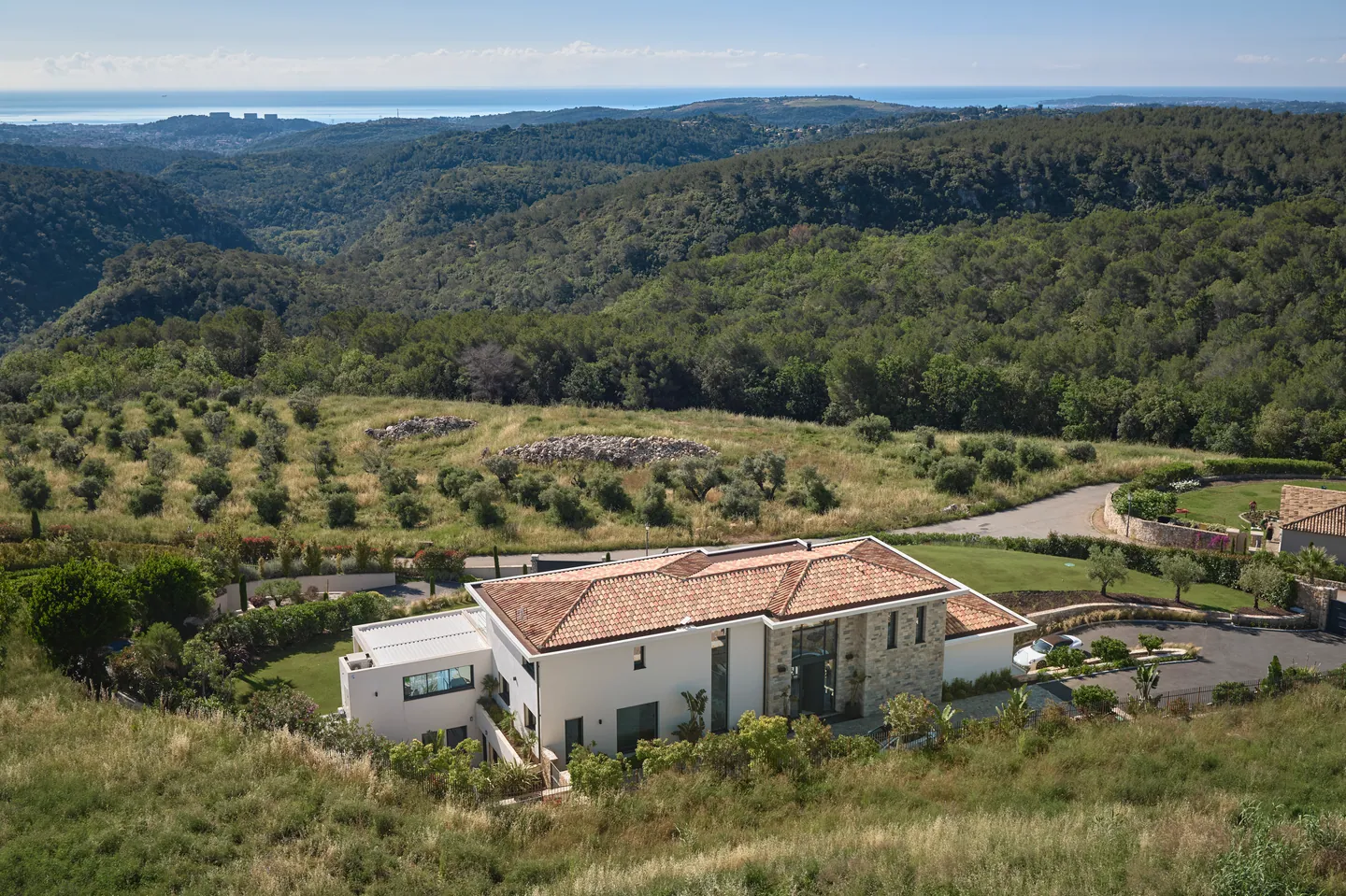 Vue aérienne de la villa côté entrée, collines boisées et mer à l'horizon
