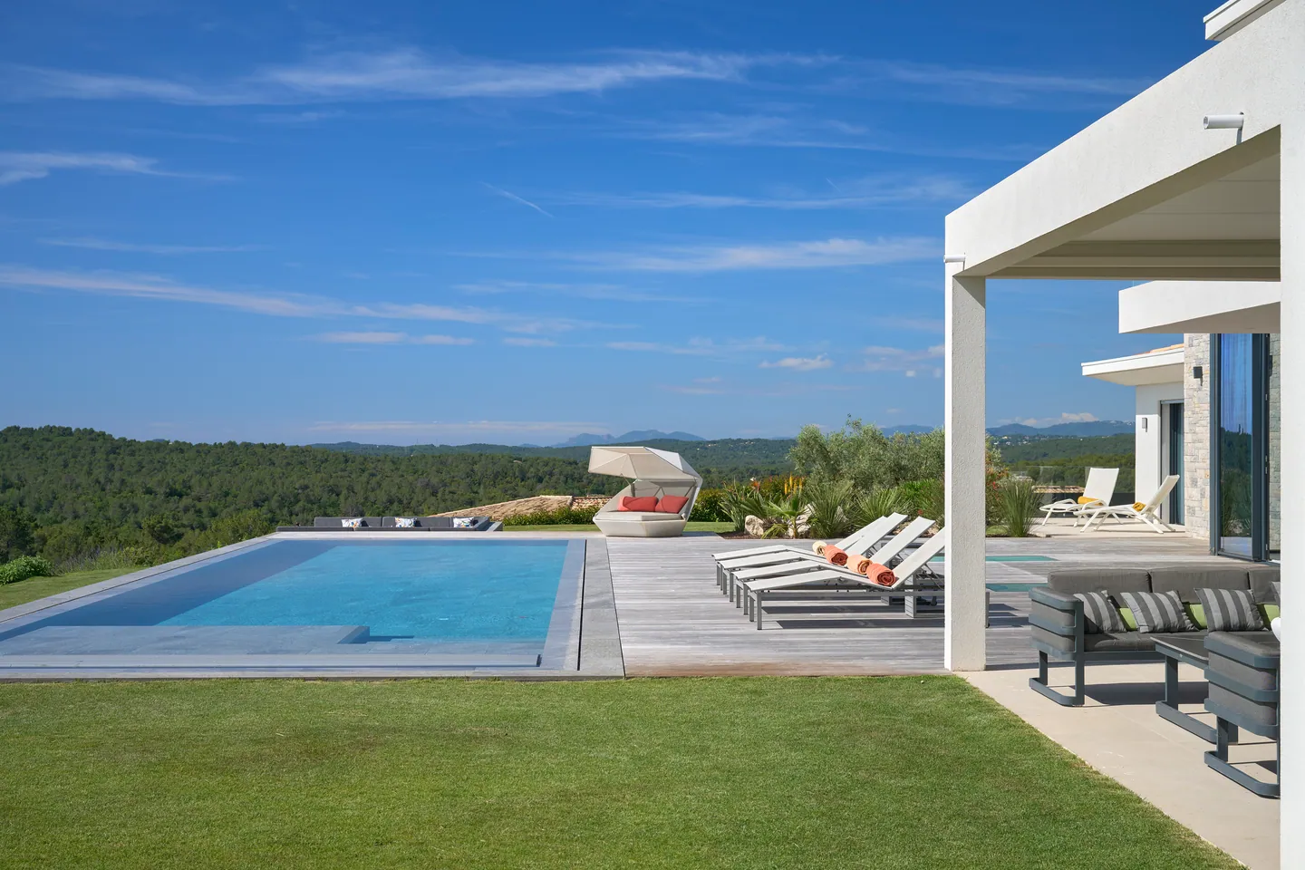 Piscine à débordement, plage en bois et transats, pelouse et collines boisées