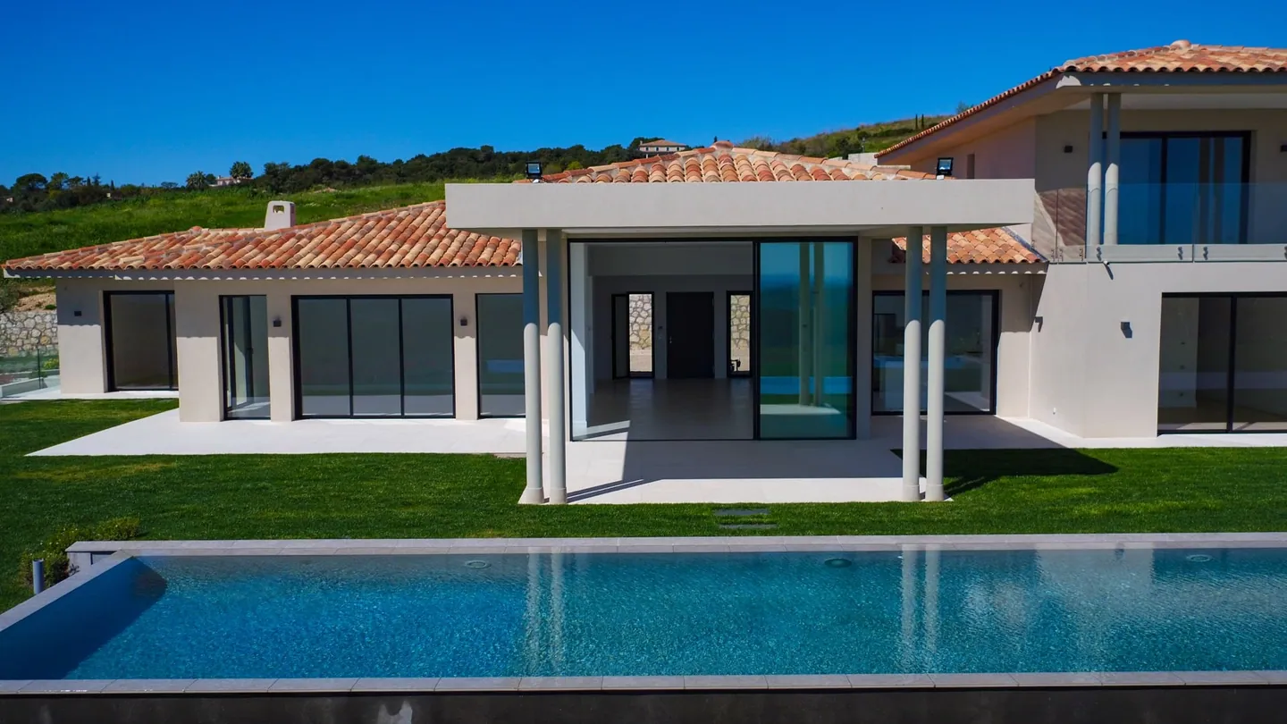 Covered terrace under a columned pergola opening onto the living area, pool in the foreground