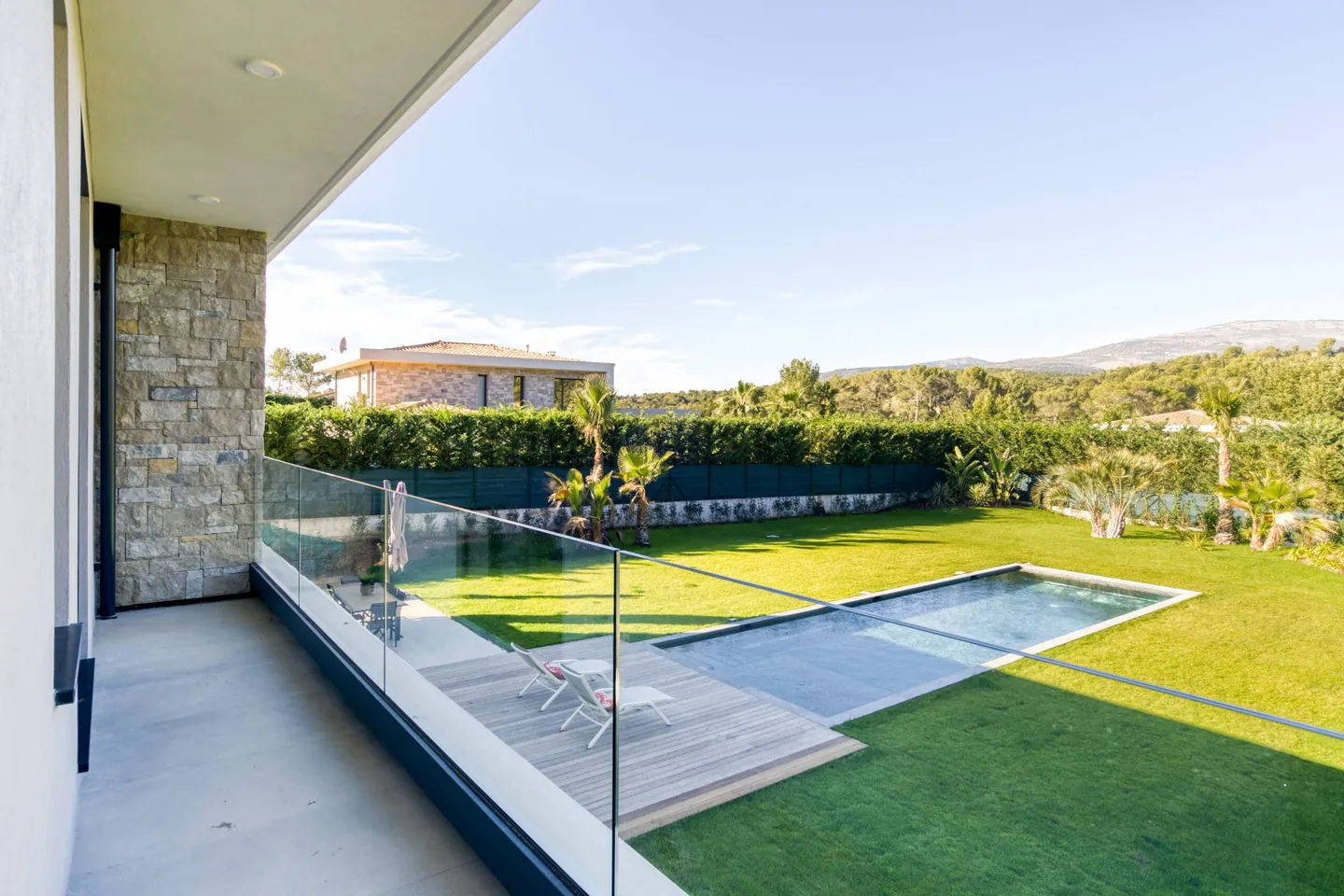 Terrasse à l'étage avec garde-corps vitré dominant la piscine, le deck en bois et le jardin
