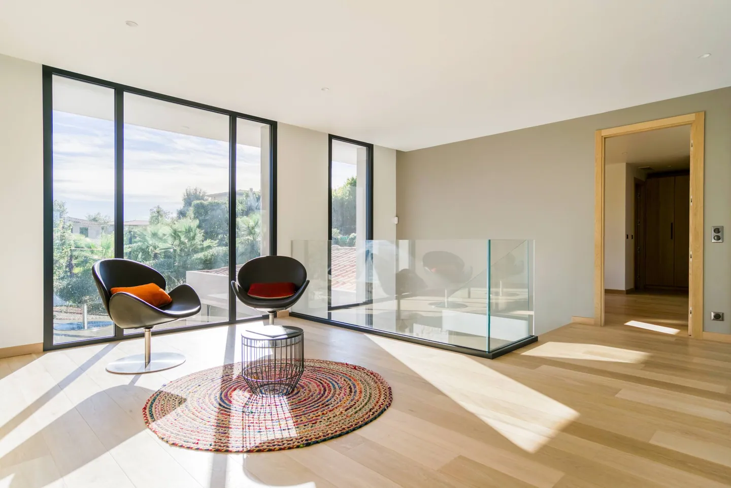 Coin détente à l'étage avec deux fauteuils, tapis rond et baies vitrées sur la végétation