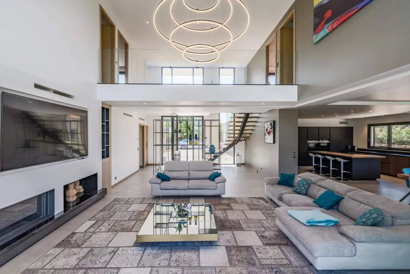 Séjour double hauteur avec mezzanine, suspension circulaire, escalier et cuisine ouverte en arrière-plan