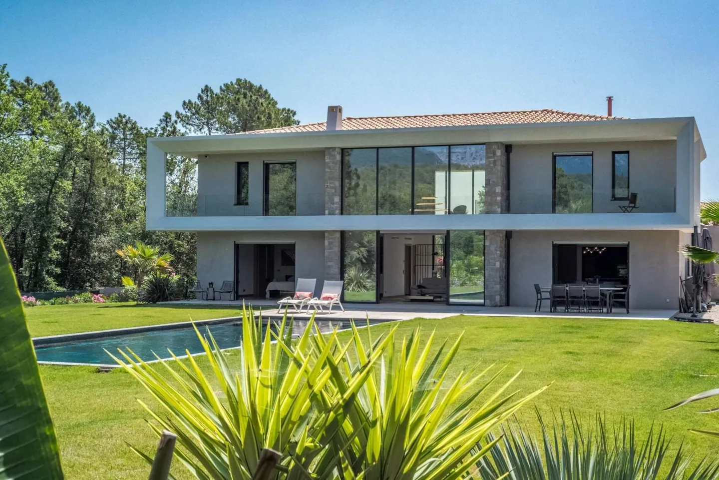 Villa contemporaine sur deux niveaux avec baies vitrées, pelouse et piscine, végétation au premier plan