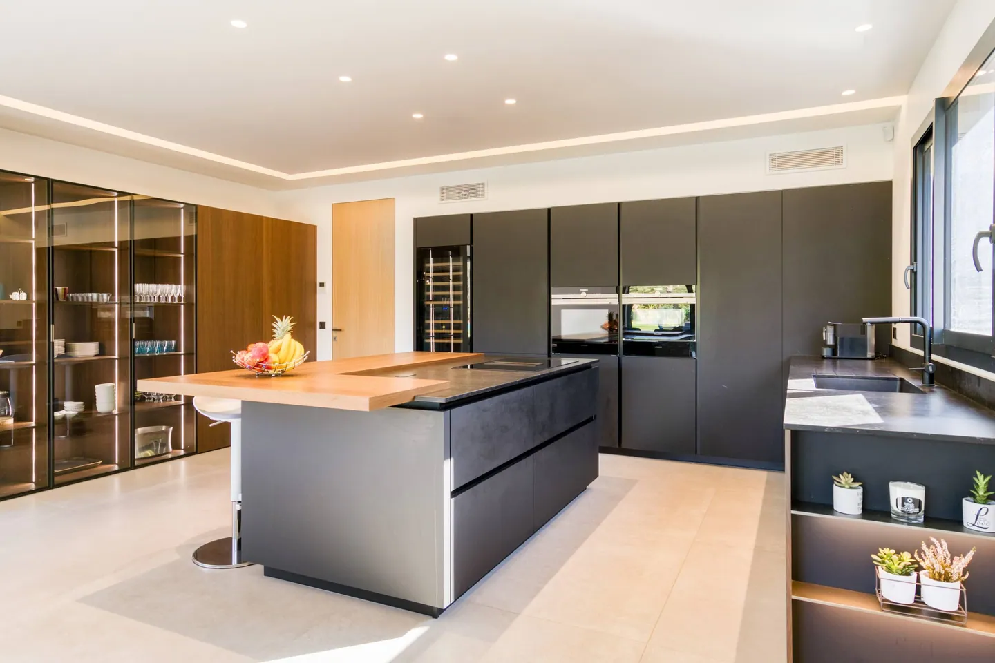 Cuisine aux façades anthracite, îlot central et vitrines éclairées pour la vaisselle
