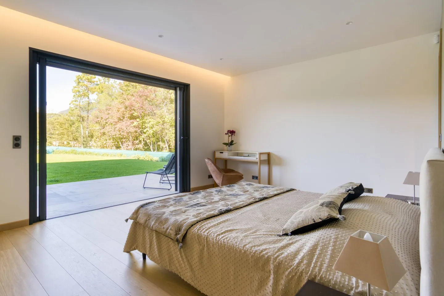 Chambre avec grand lit et baie vitrée ouverte sur une terrasse et le jardin arboré