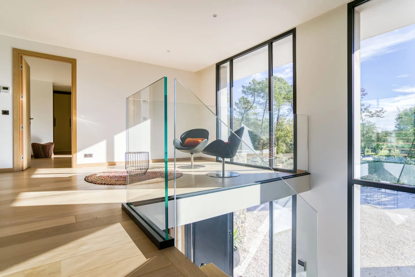 Mezzanine lumineuse avec fauteuils, garde-corps en verre et vue plongeante sur l'entrée