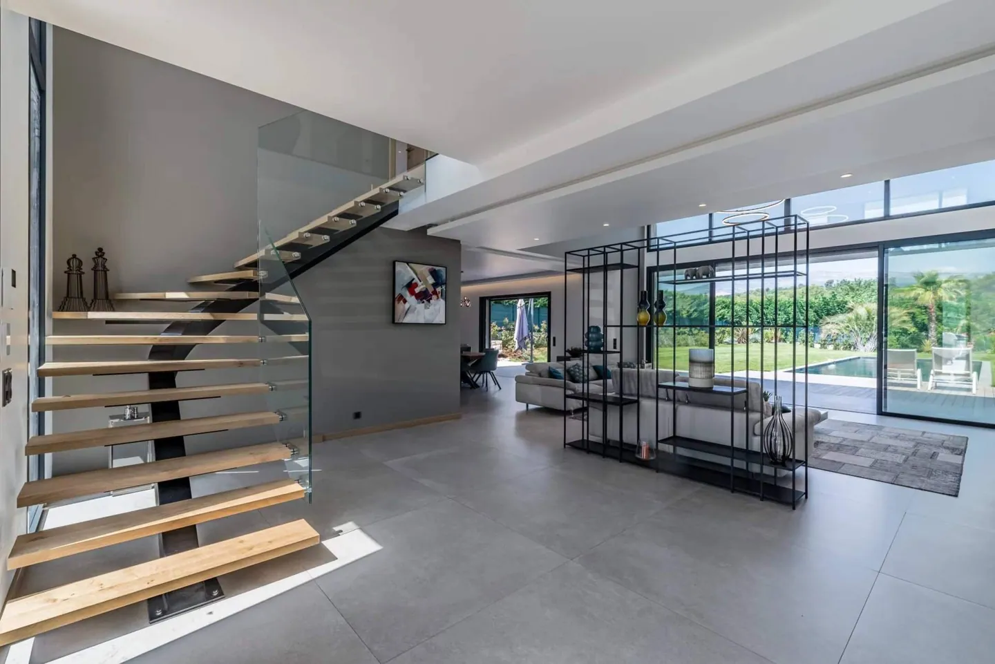 Hall d'entrée avec escalier suspendu en bois et verre, séjour ouvert sur la piscine