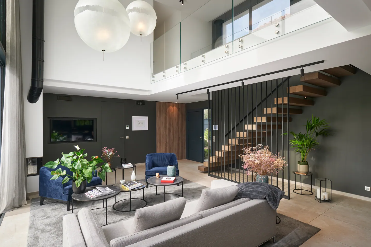 Salon avec canapé gris et fauteuils en velours bleu face à l'escalier à claire-voie