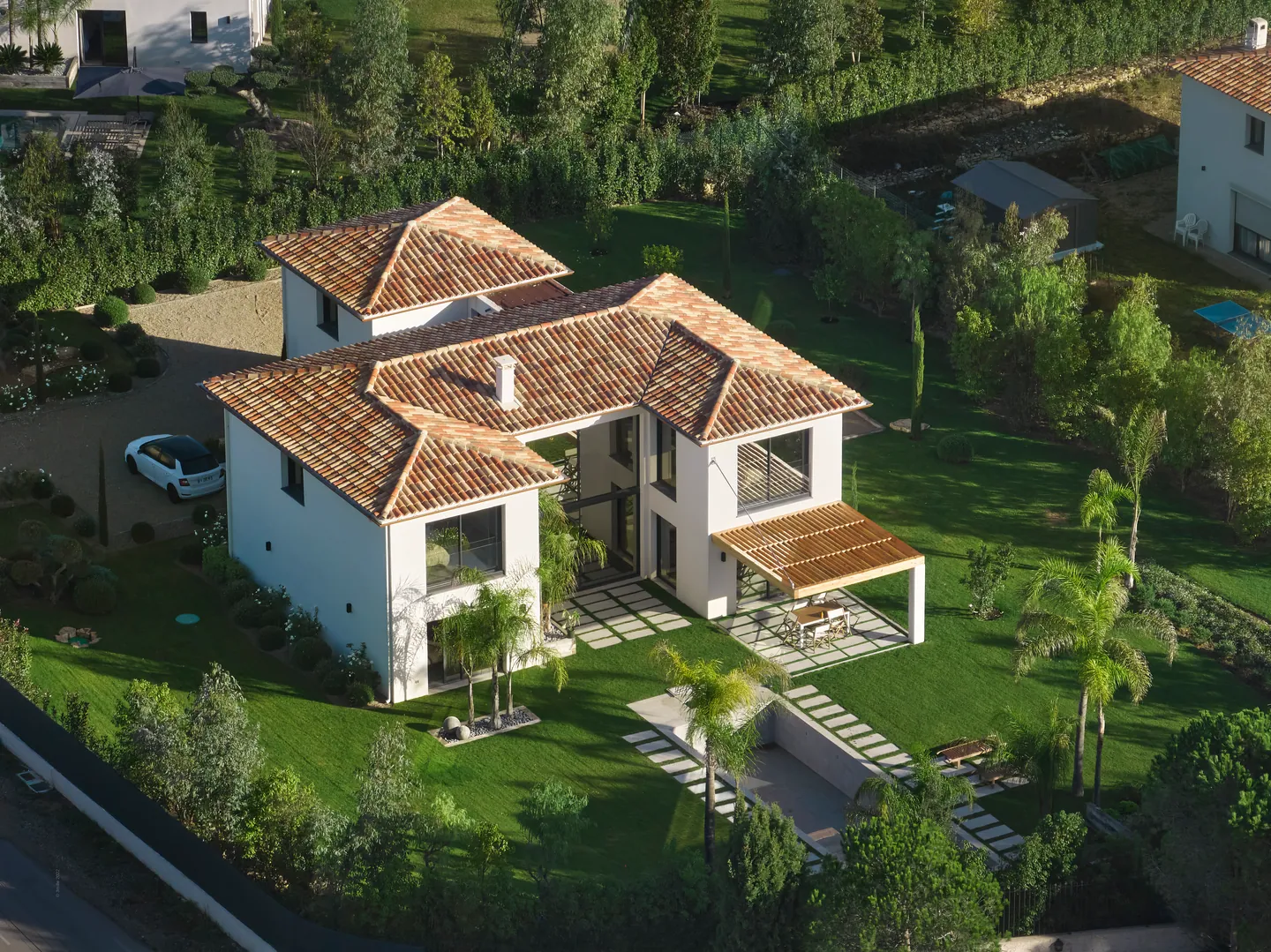 Vue aérienne de la villa, de ses toits de tuiles, de sa pergola et de son jardin planté de palmiers