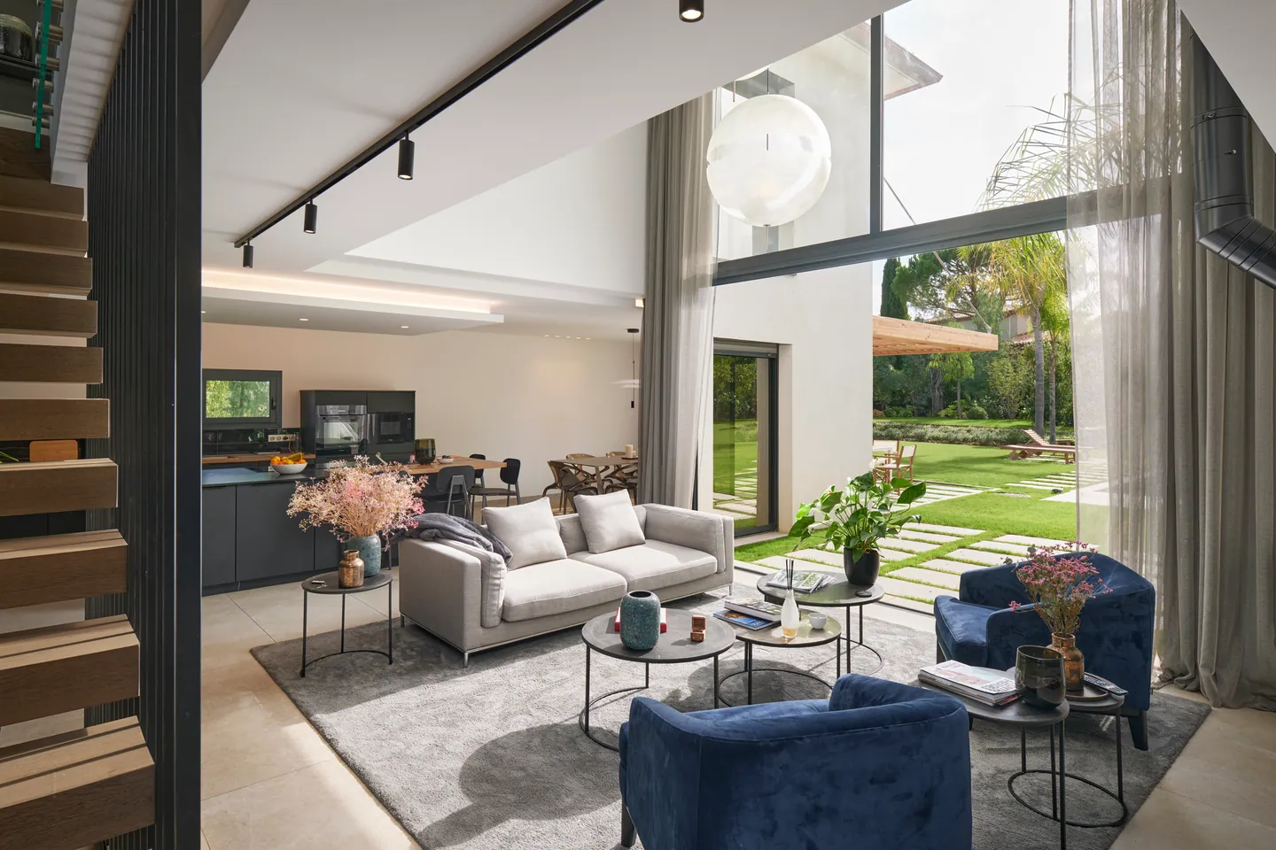 Salon ouvert sur le jardin par de grandes baies, fauteuils bleus et cuisine au fond
