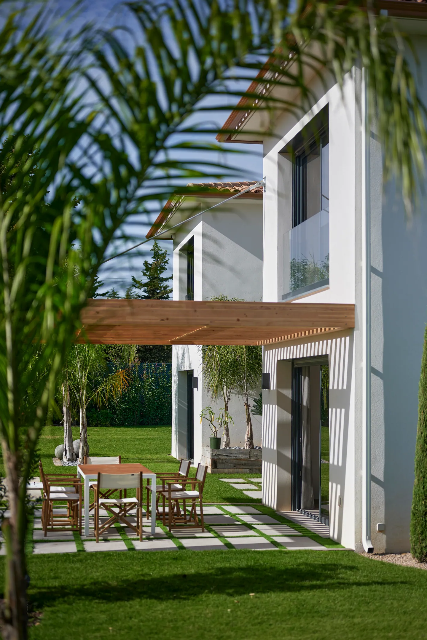 Terrasse sous pergola en bois avec table et chaises de jardin, dalles posées dans la pelouse