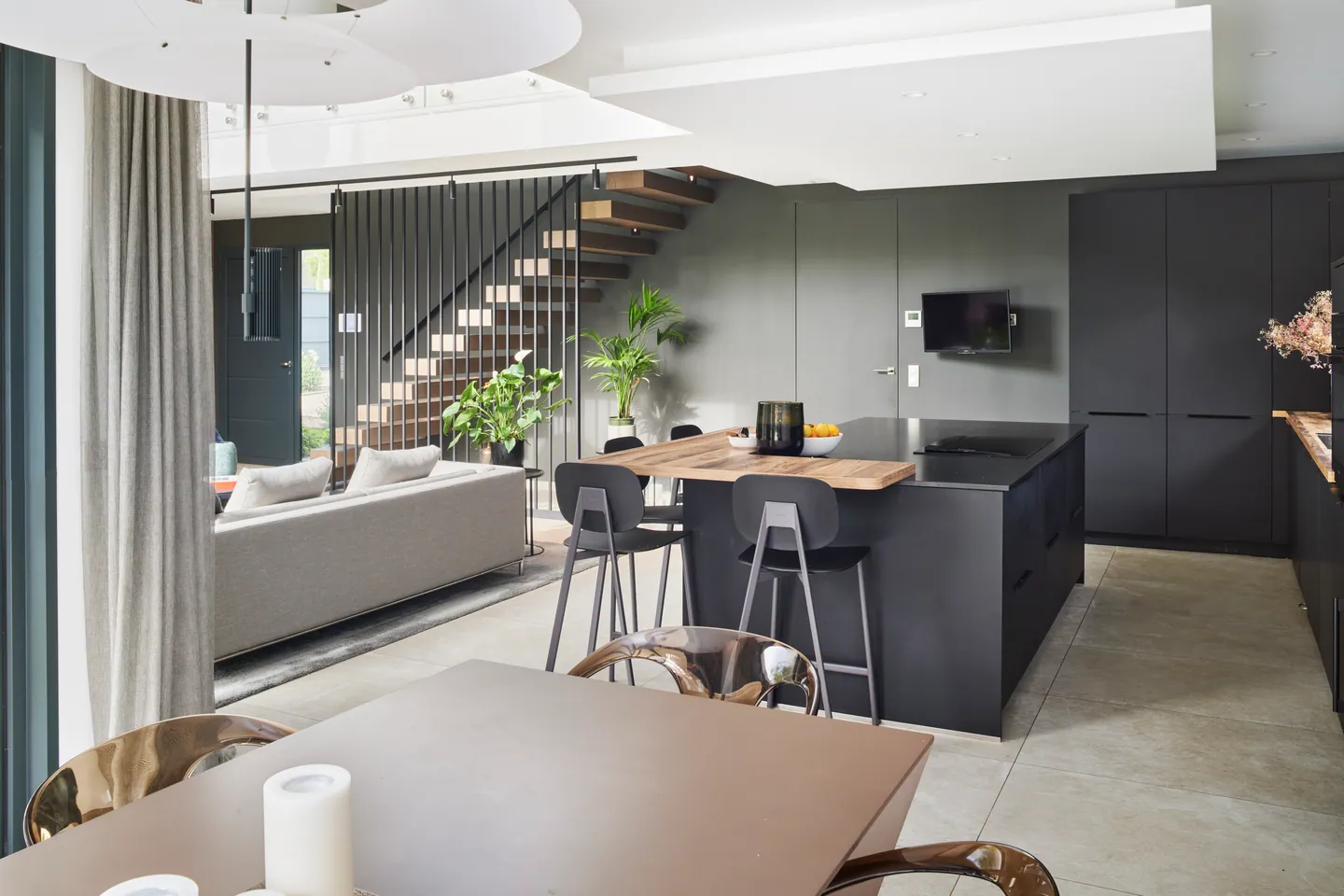 Cuisine anthracite avec îlot et comptoir en bois, tabourets hauts et escalier en arrière-plan