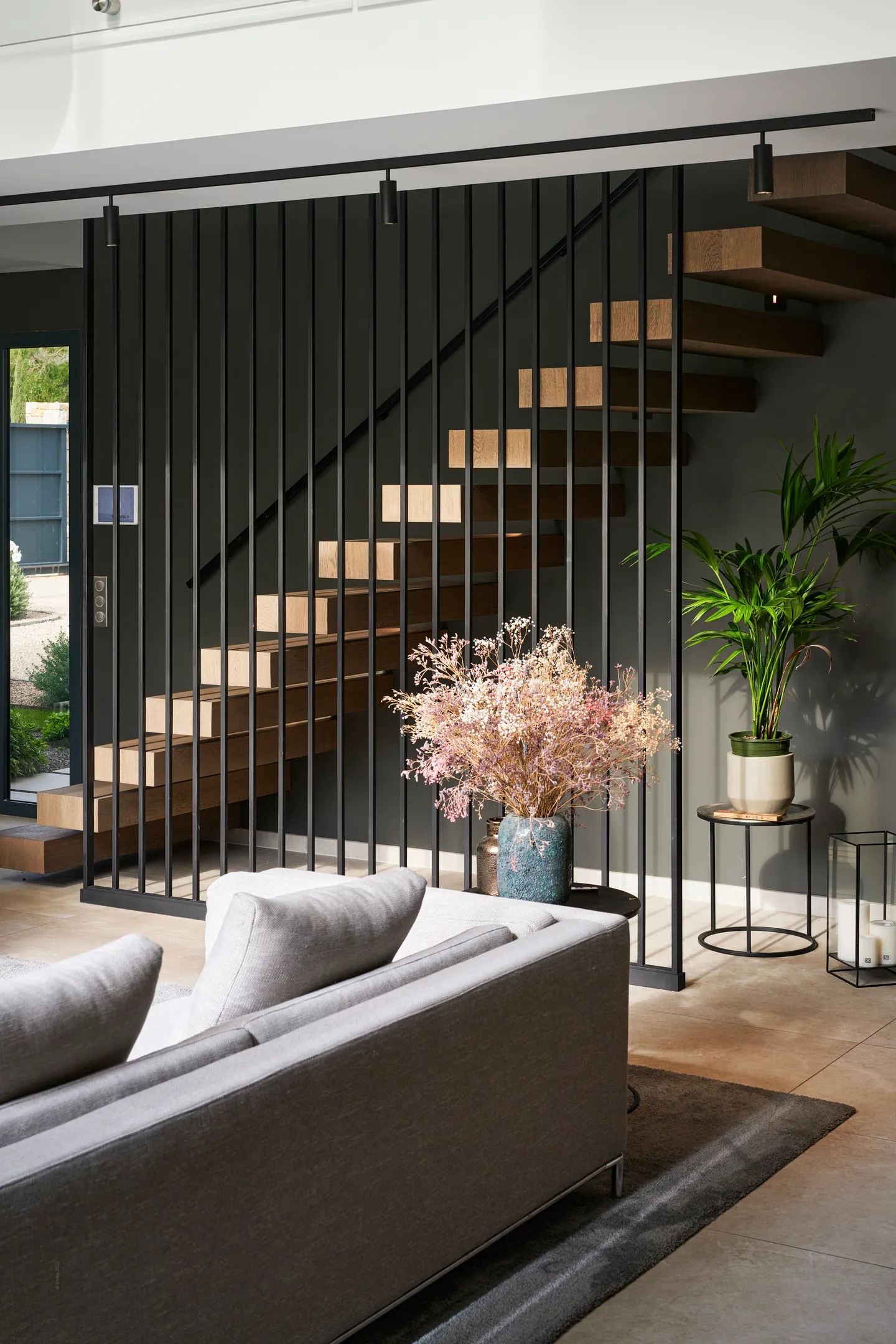 Escalier en bois à claire-voie derrière des barreaux métalliques noirs, plantes et fleurs séchées