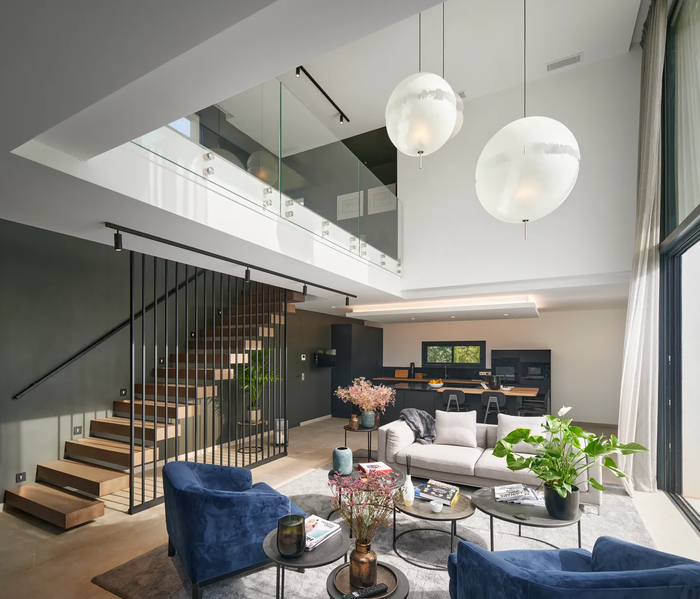 Séjour double hauteur avec escalier suspendu, suspensions globes et cuisine en arrière-plan