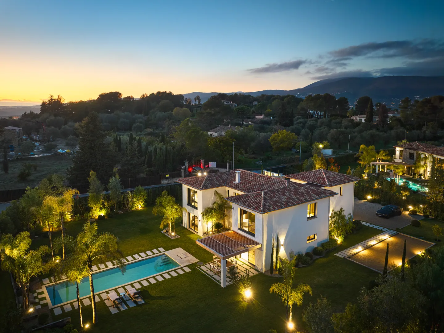 Vue aérienne au coucher du soleil : villa illuminée, piscine et collines à l'horizon