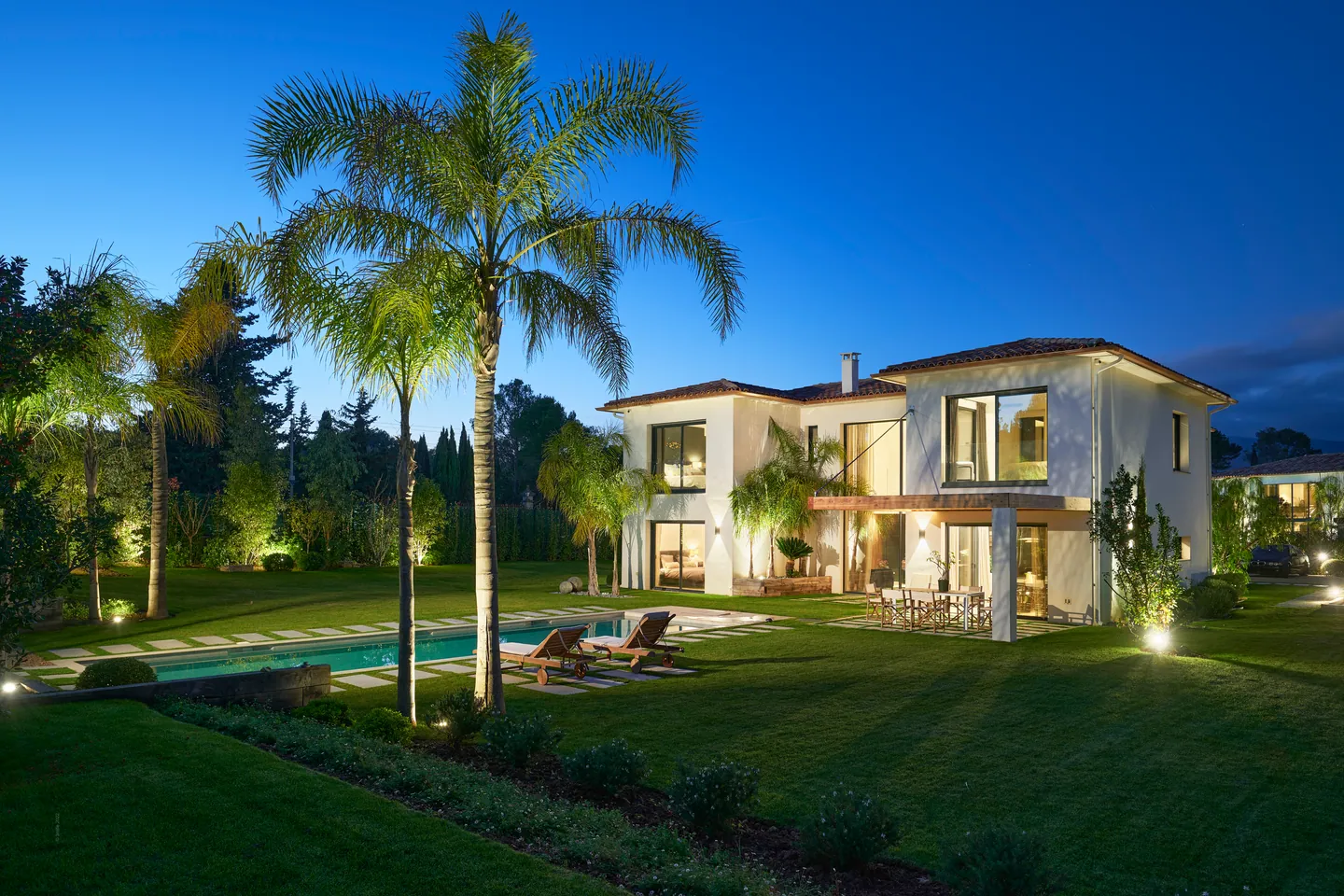 Villa et jardin illuminés à l'heure bleue, palmiers et piscine au premier plan