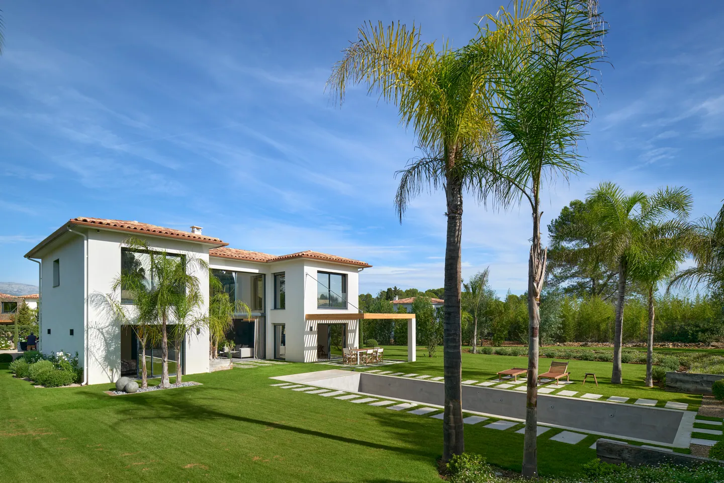 Jardin paysager avec palmiers, piscine encastrée et transats devant la villa