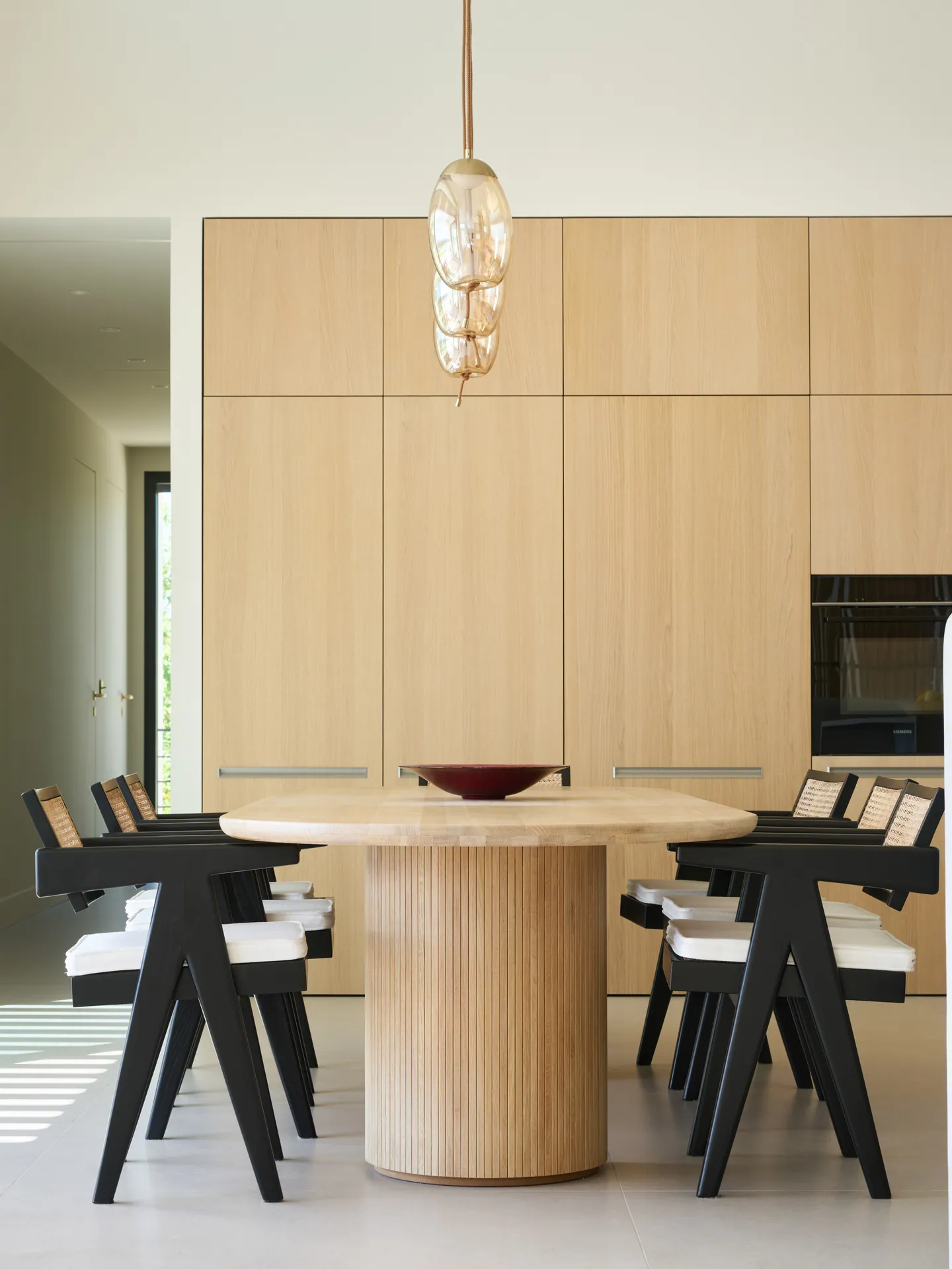 Table en chêne au pied cannelé sous une suspension en verre, chaises cannées noires