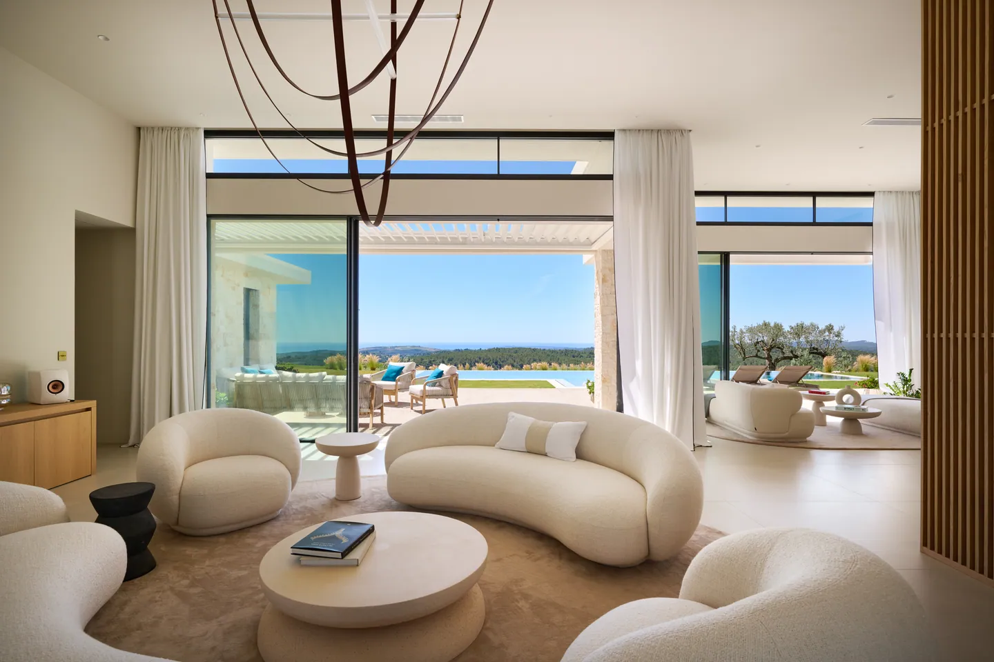 Salon aux canapés bouclette arrondis, baies vitrées ouvertes sur la terrasse et la vue mer