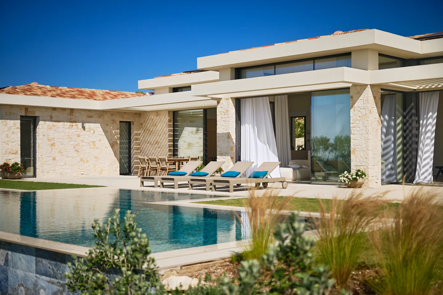 Transats au bord de la piscine devant la loggia aux voilages blancs