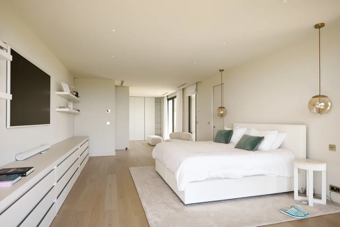 Chambre parentale, lit blanc, suspensions en verre ambré et meuble bas sur toute la longueur