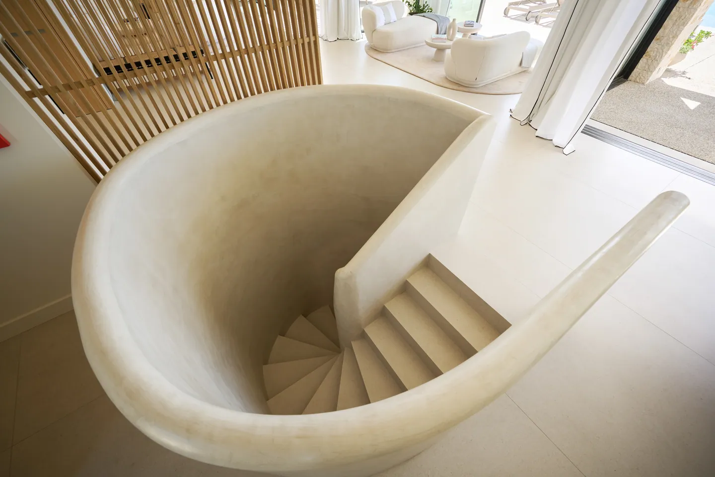 Escalier hélicoïdal aux parois arrondies en enduit minéral, vu depuis le séjour