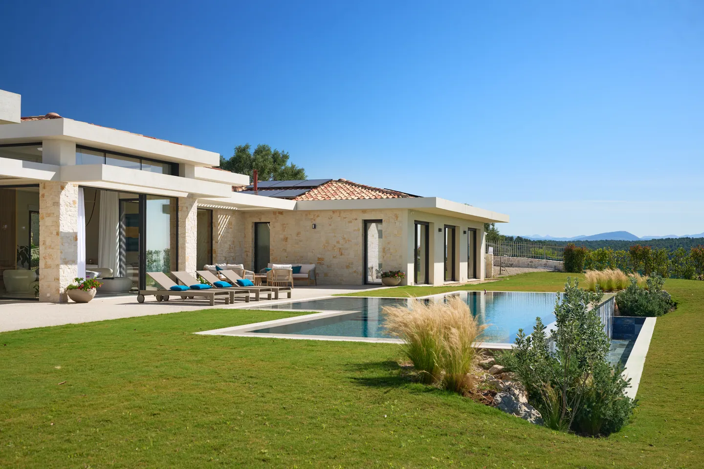 Aile de la villa en pierre et enduit, transats sur la terrasse le long de la piscine