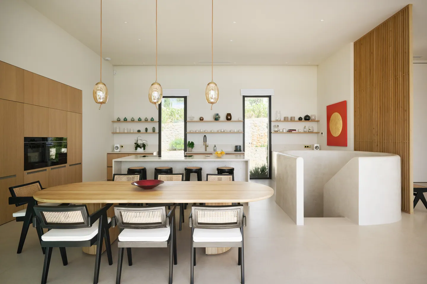 Cuisine ouverte avec îlot, étagères en chêne et table à manger, escalier sculpté à droite