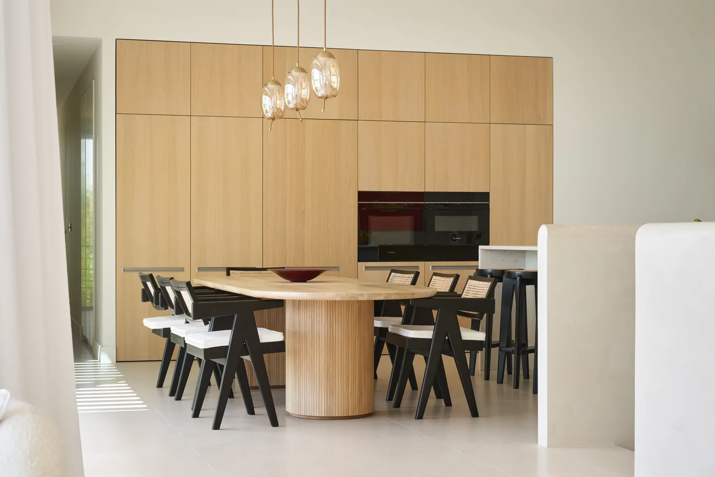 Table ovale sur pied cannelé, chaises cannées noires et mur de rangements en chêne