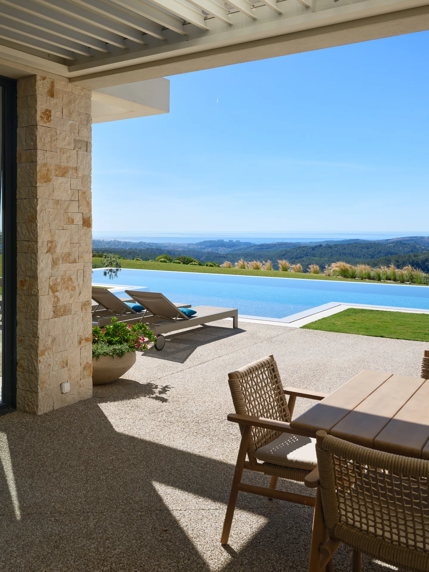 Terrasse couverte avec table et chaises en corde, piscine à débordement et vue mer