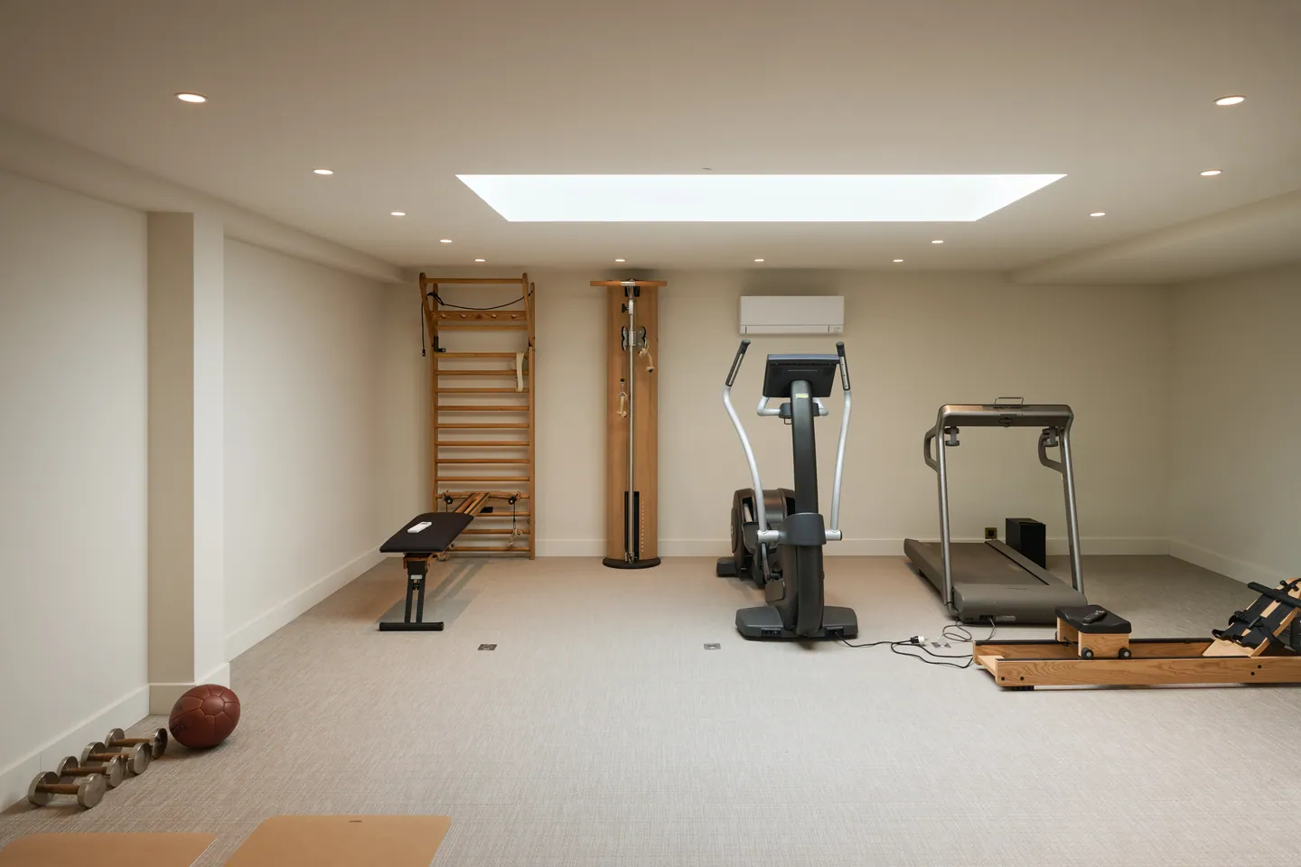 Salle de sport éclairée par un puits de lumière, espalier, tapis de course et vélo elliptique
