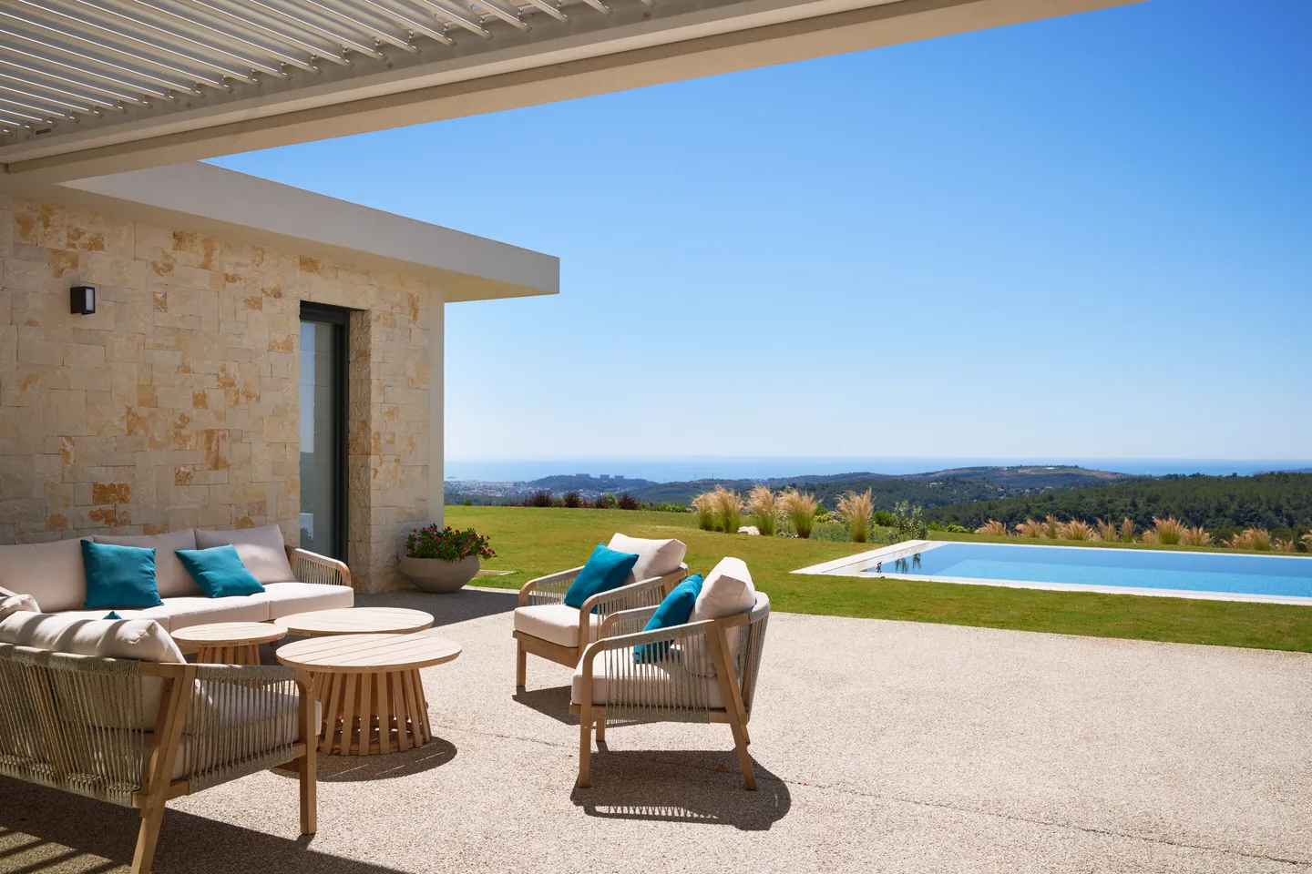 Salon de terrasse face à la mer, fauteuils en corde, piscine et graminées en contrebas