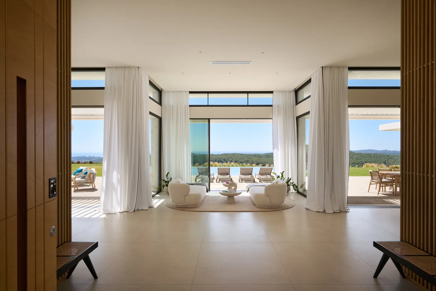 Hall ouvert sur le salon et la terrasse, grands voilages, vue sur la piscine et les collines