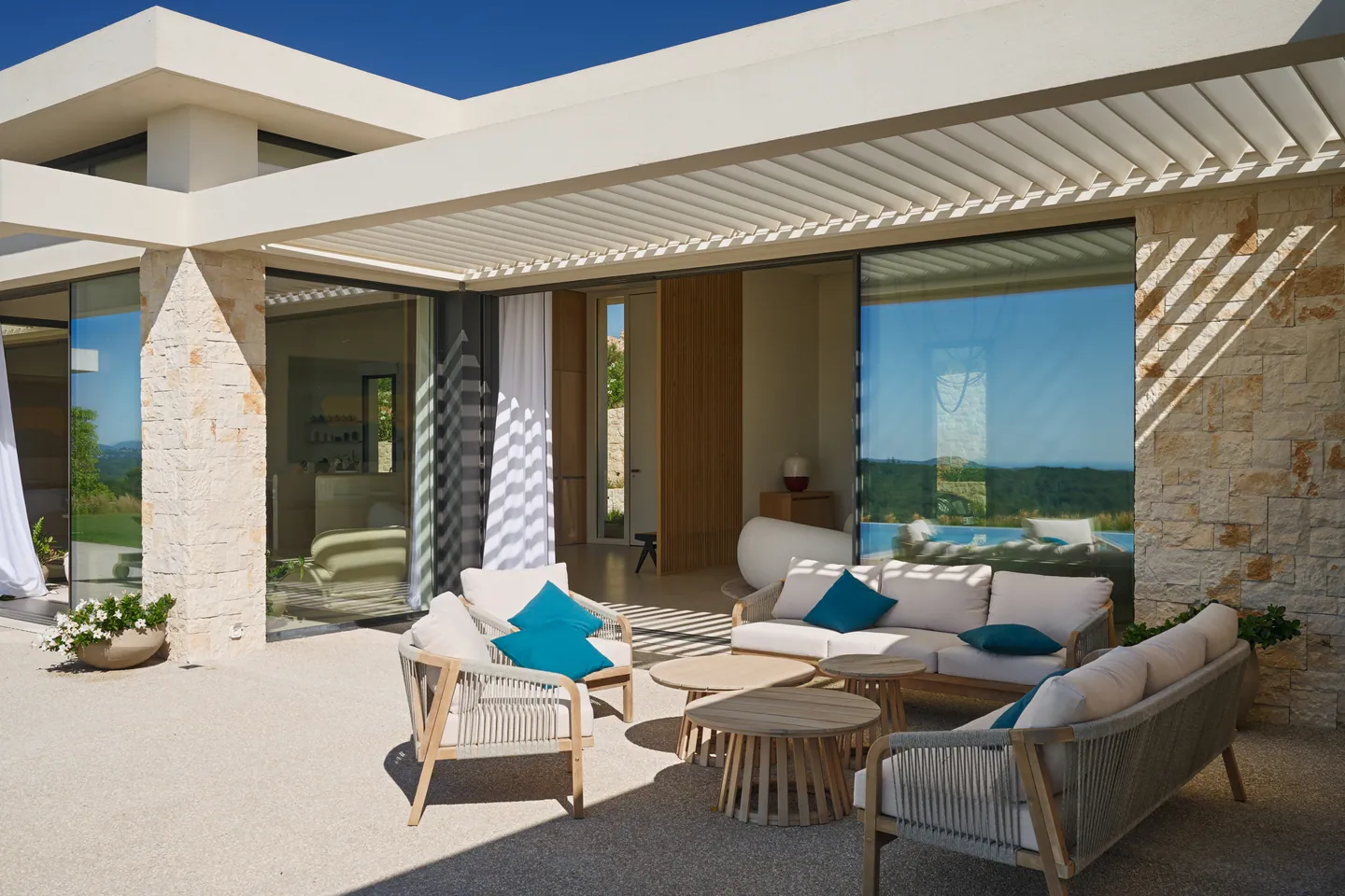 Salon extérieur en bois et corde sous pergola à lames orientables, coussins bleu canard