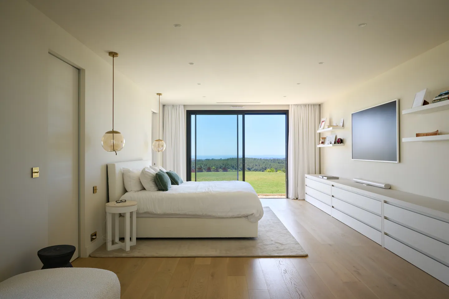 Chambre parentale lumineuse, lit blanc face à une baie ouverte sur le jardin et les collines