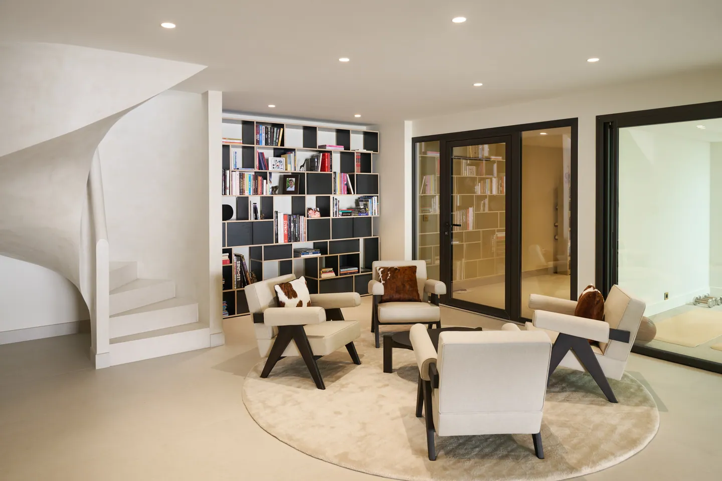 Salon bibliothèque avec quatre fauteuils sur tapis rond, escalier hélicoïdal blanc