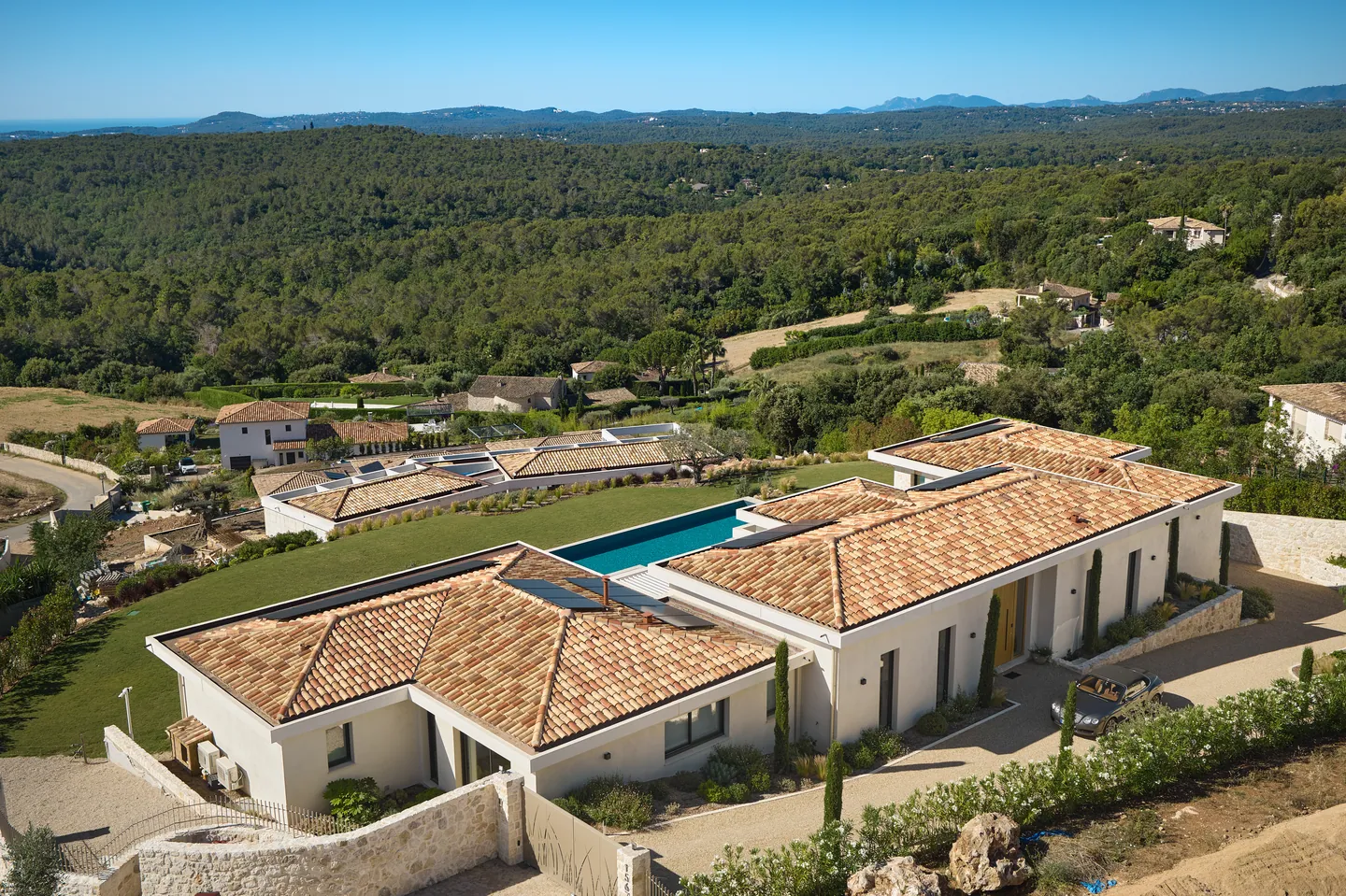 Vue aérienne de la villa et de sa piscine au milieu des collines boisées, mer à l'horizon
