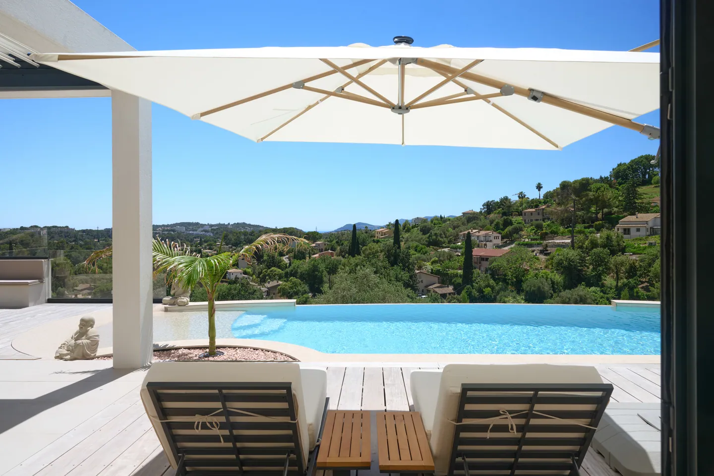 Transats sous un grand parasol face à la piscine à débordement et au panorama vallonné