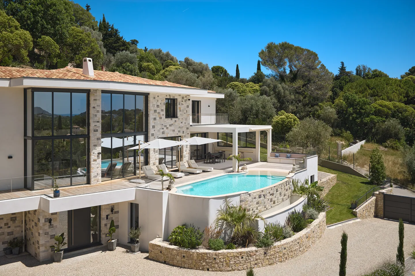 Piscine à débordement et terrasse de transats devant la façade vitrée, collines boisées en arrière-plan