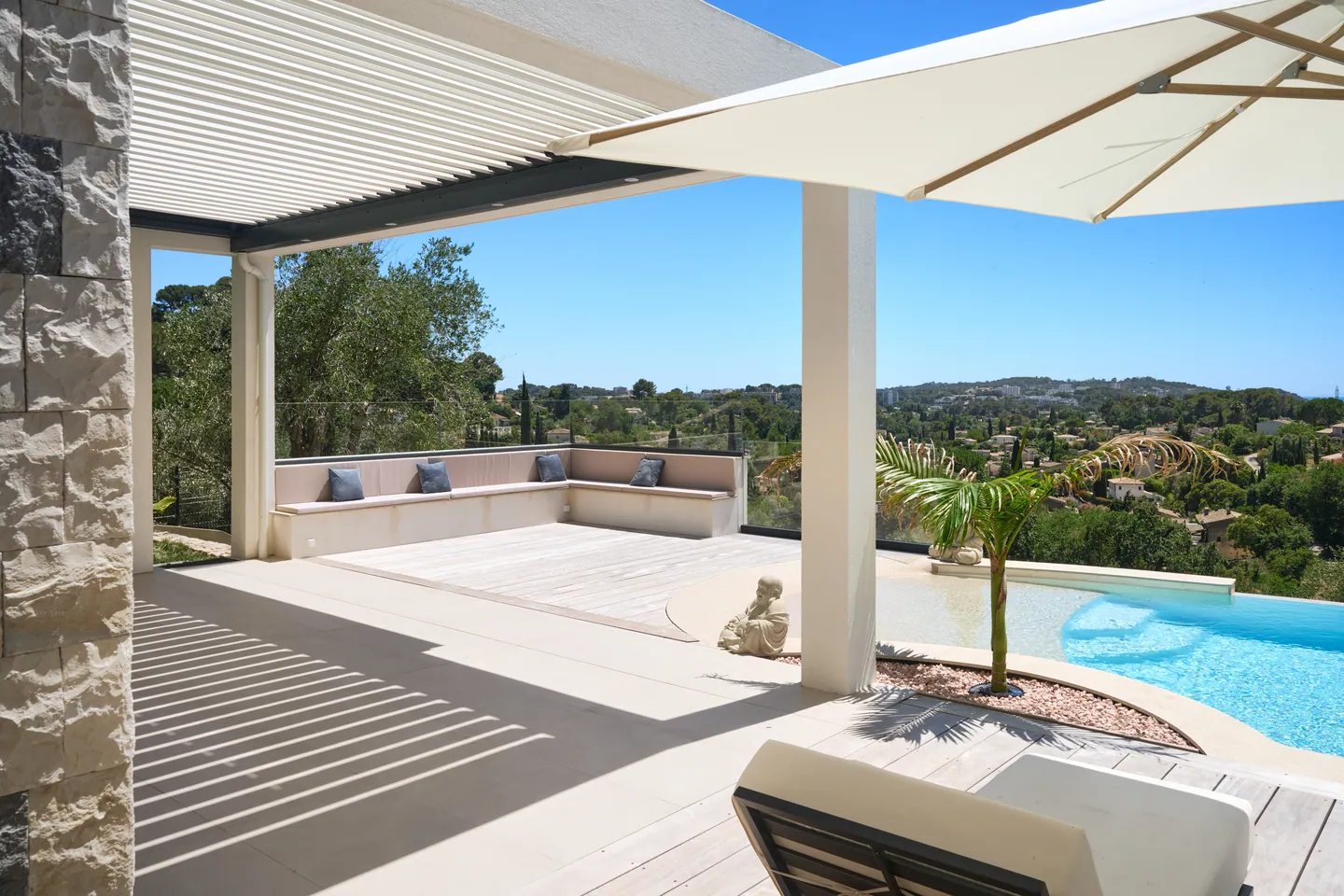 Terrasse sous pergola à lames, banquette coussinée et piscine à débordement ouverte sur la vue