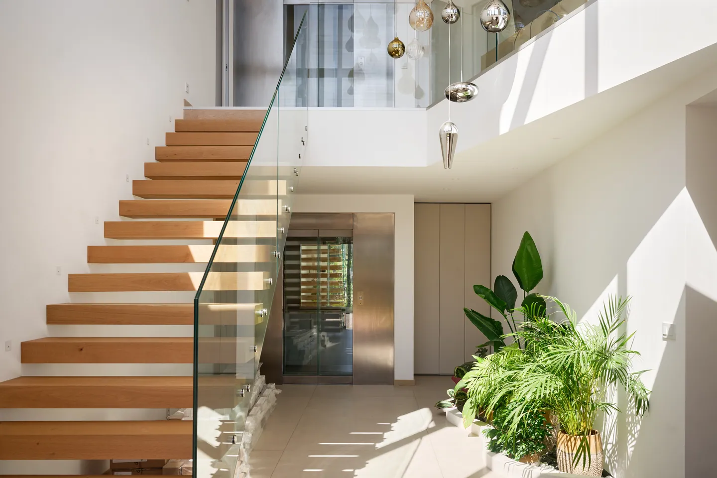 Hall d'entrée avec escalier à marches suspendues, garde-corps en verre et plantes tropicales