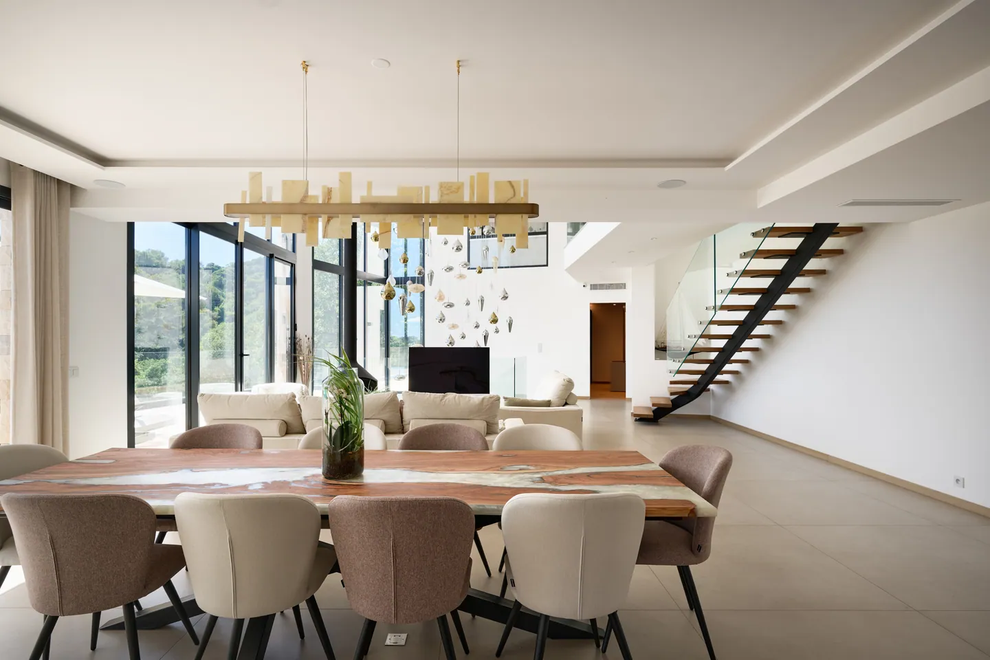 Table en bois et résine sous un lustre aux pavés translucides, salon et escalier en arrière-plan