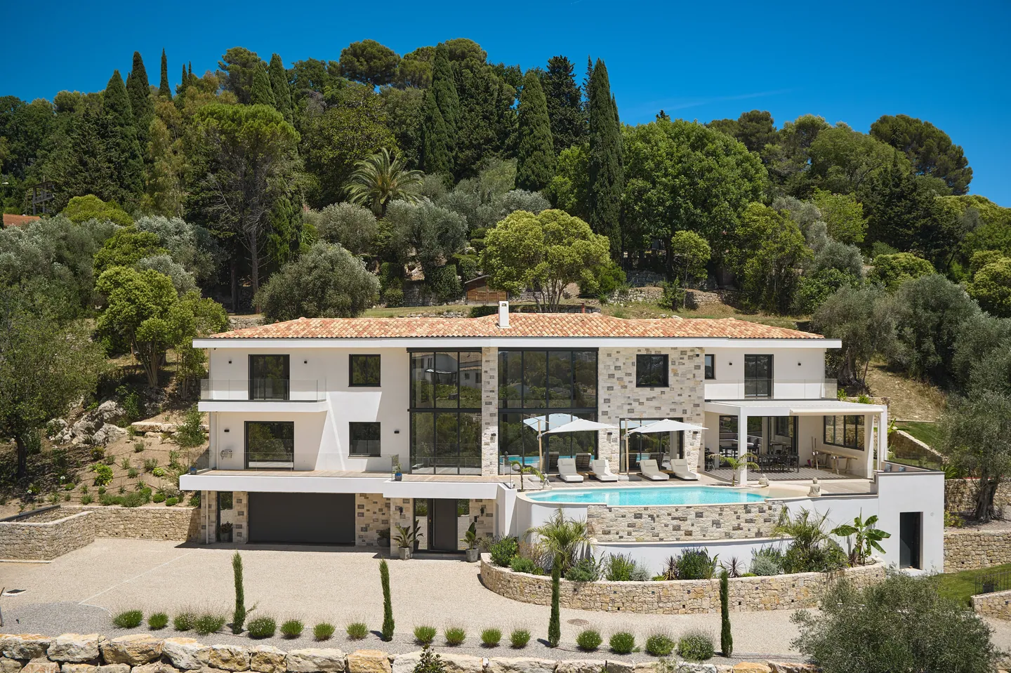 Villa contemporaine en pierre et enduit blanc, piscine en surplomb et cour gravillonnée au pied des pins