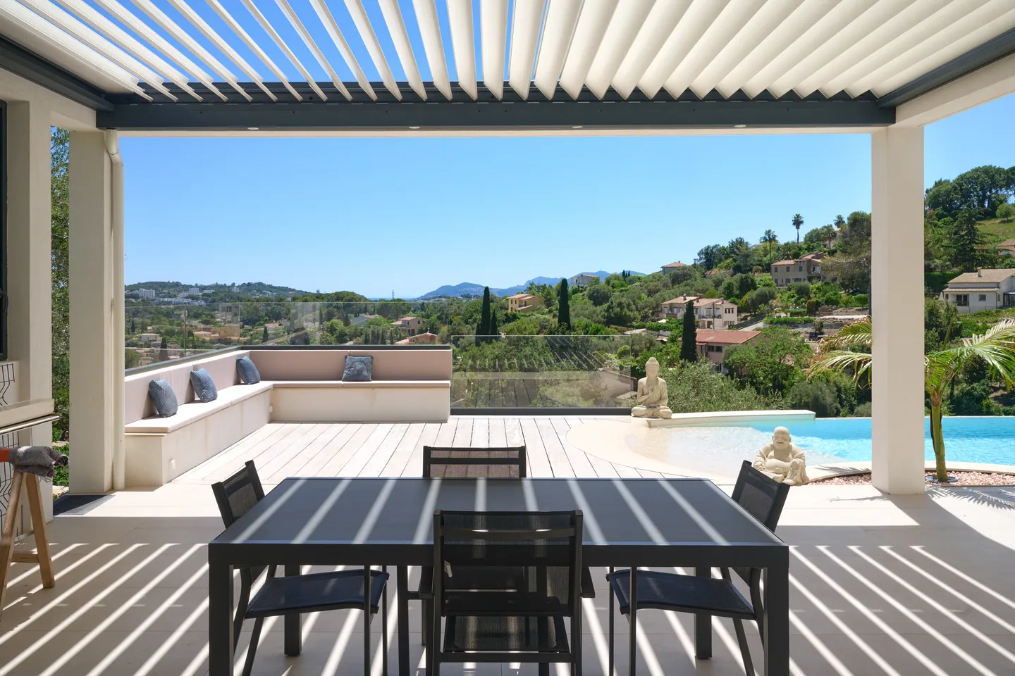 Pergola bioclimatique abritant une table à manger, banquette maçonnée et bord de piscine