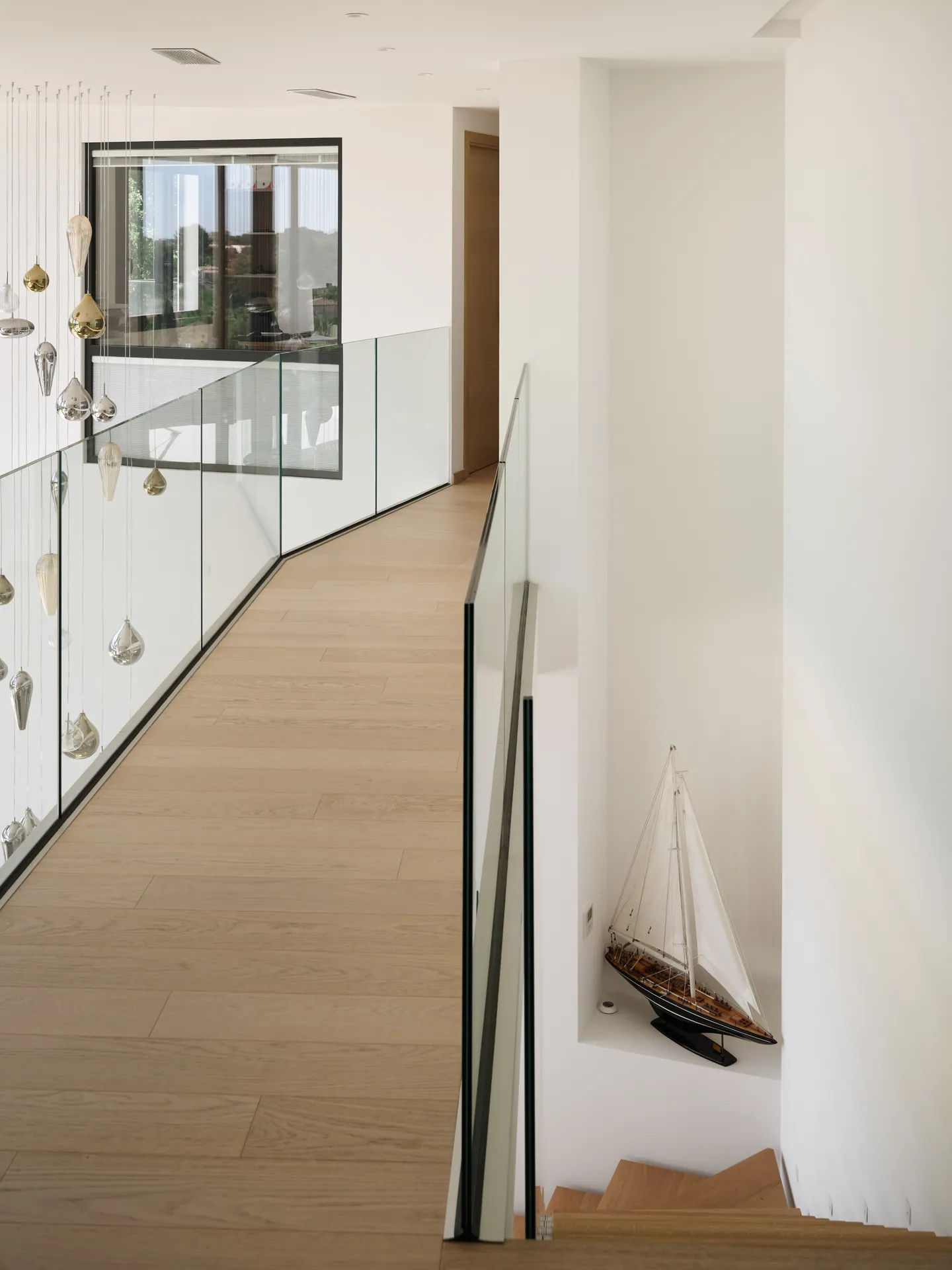 Coursive de mezzanine en parquet bordée de verre, maquette de voilier dans une niche