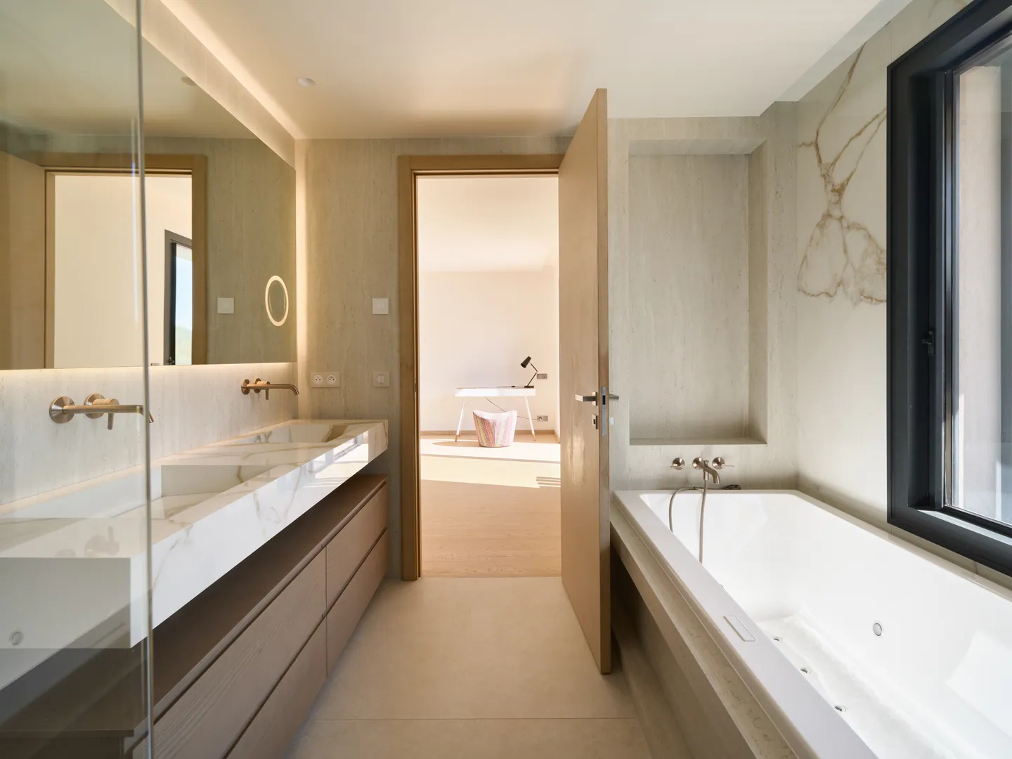 Salle de bains avec double vasque en marbre, robinetterie dorée et baignoire sous la fenêtre