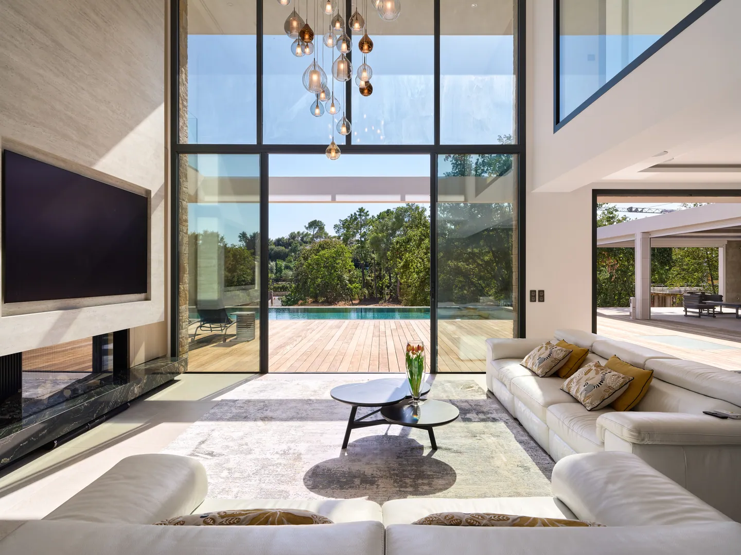 Séjour double hauteur avec lustre en verre soufflé, verrière ouverte sur le deck et la piscine